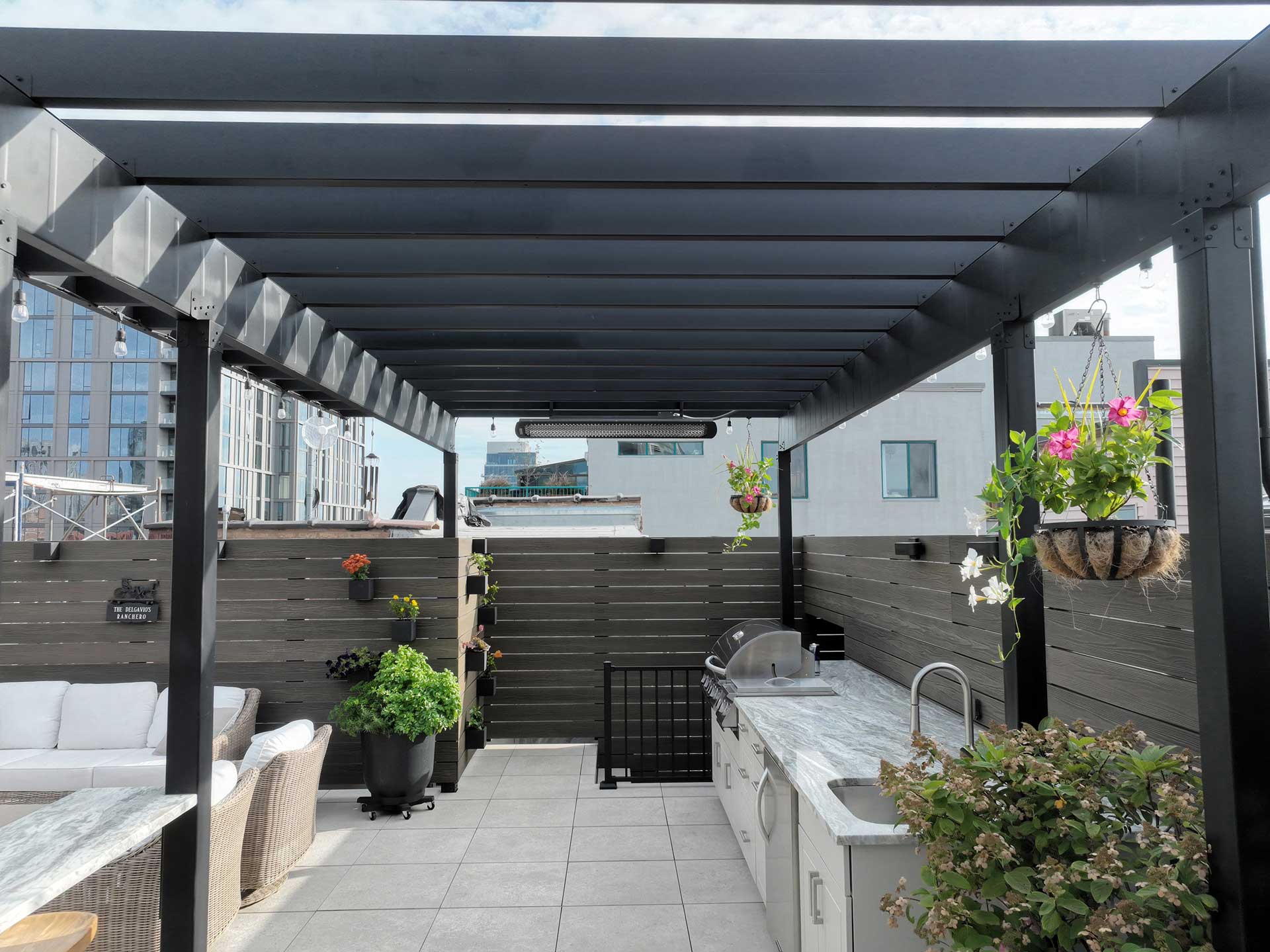 Urban outdoor kitchen under a sleek steel pergola, with integrated lighting and hanging plants
