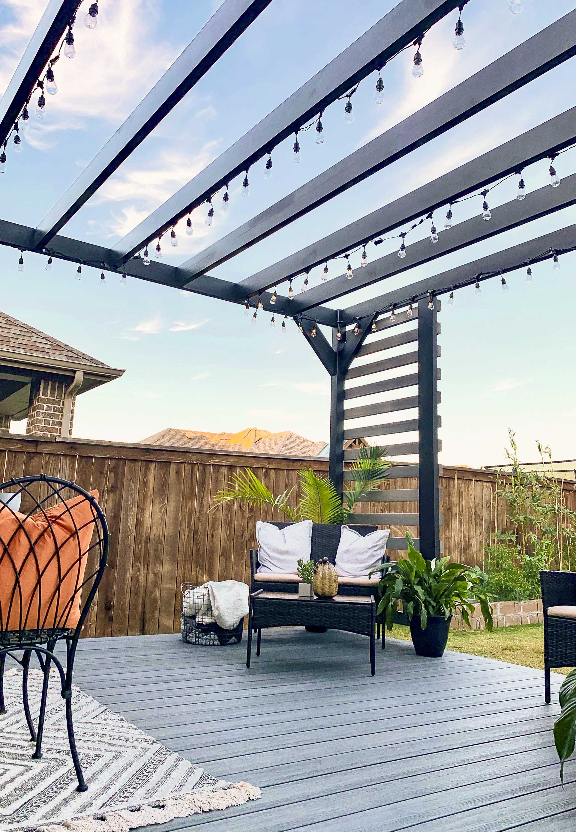 Cozy backyard with steel pergola adorned with string lights, seating area, and potted plants