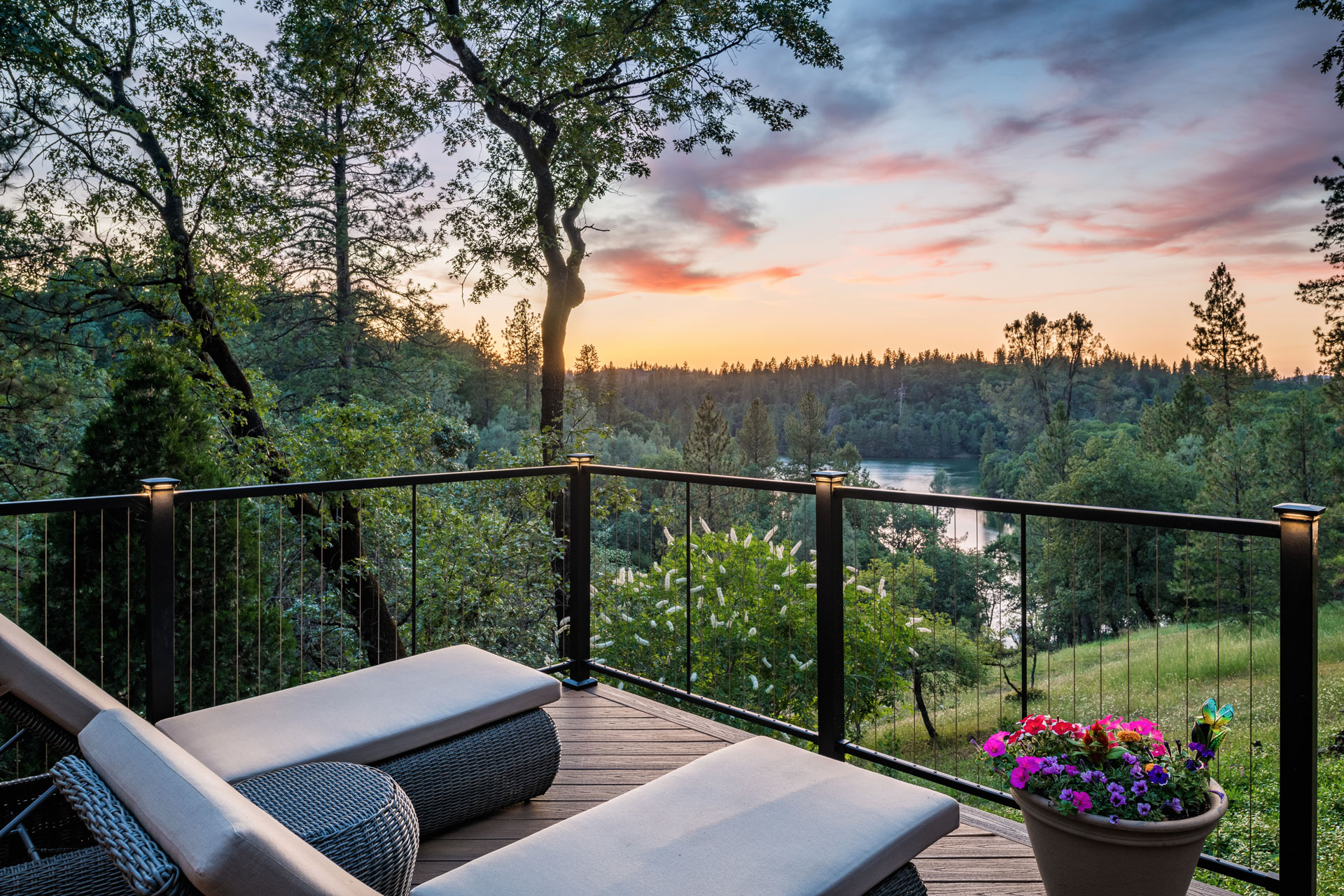 View from deck of the sunset over a lake with patio chairs and cable railing surrounding the deck.
